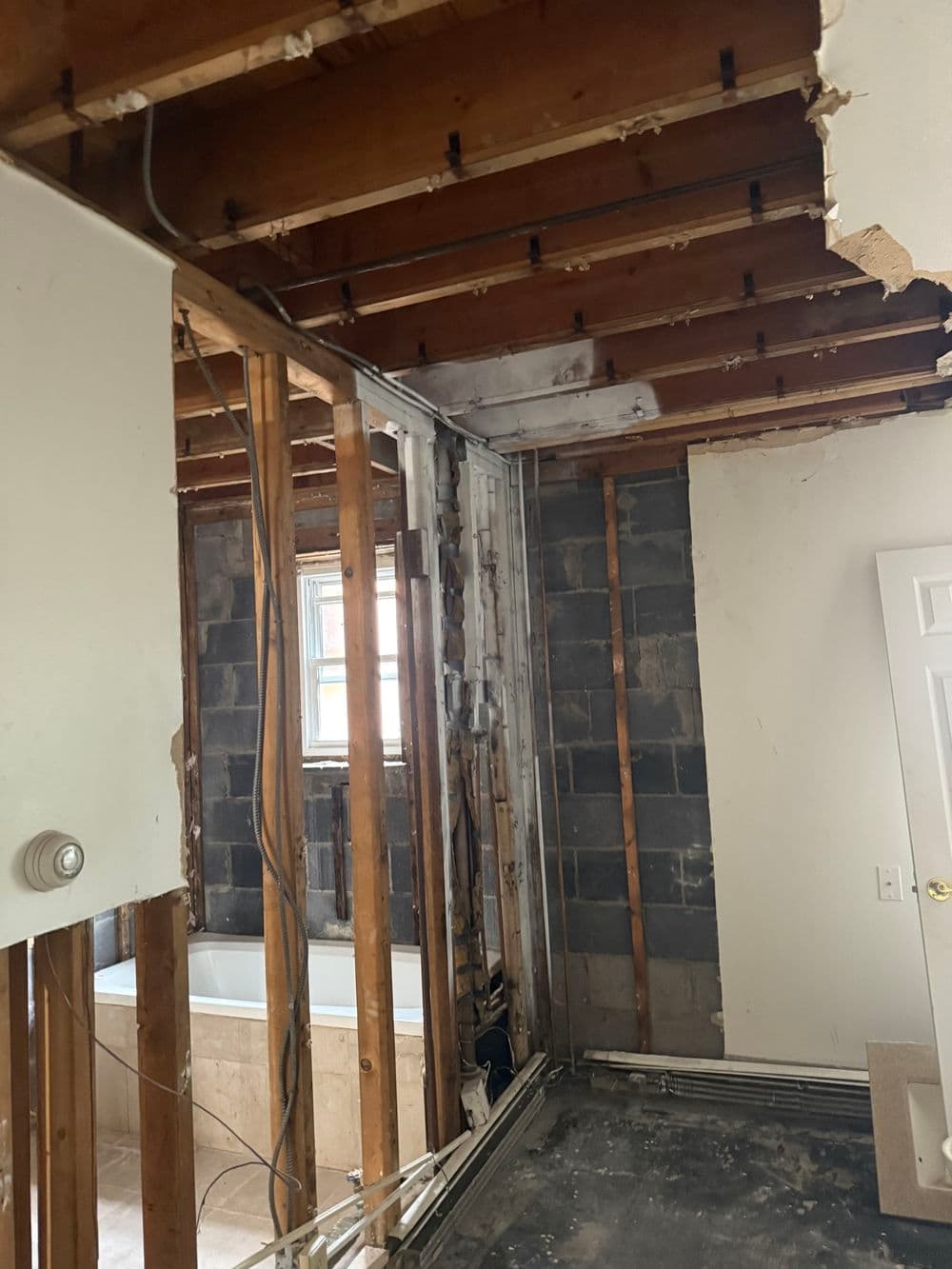 Renovation project showing exposed walls, ceiling beams, and plumbing in an unfinished room.