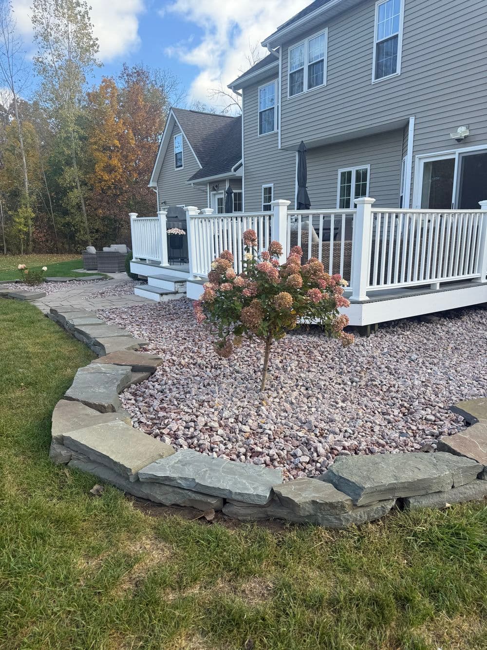 Landscape featuring a stone-bordered garden with a flowering tree and a two-story home.