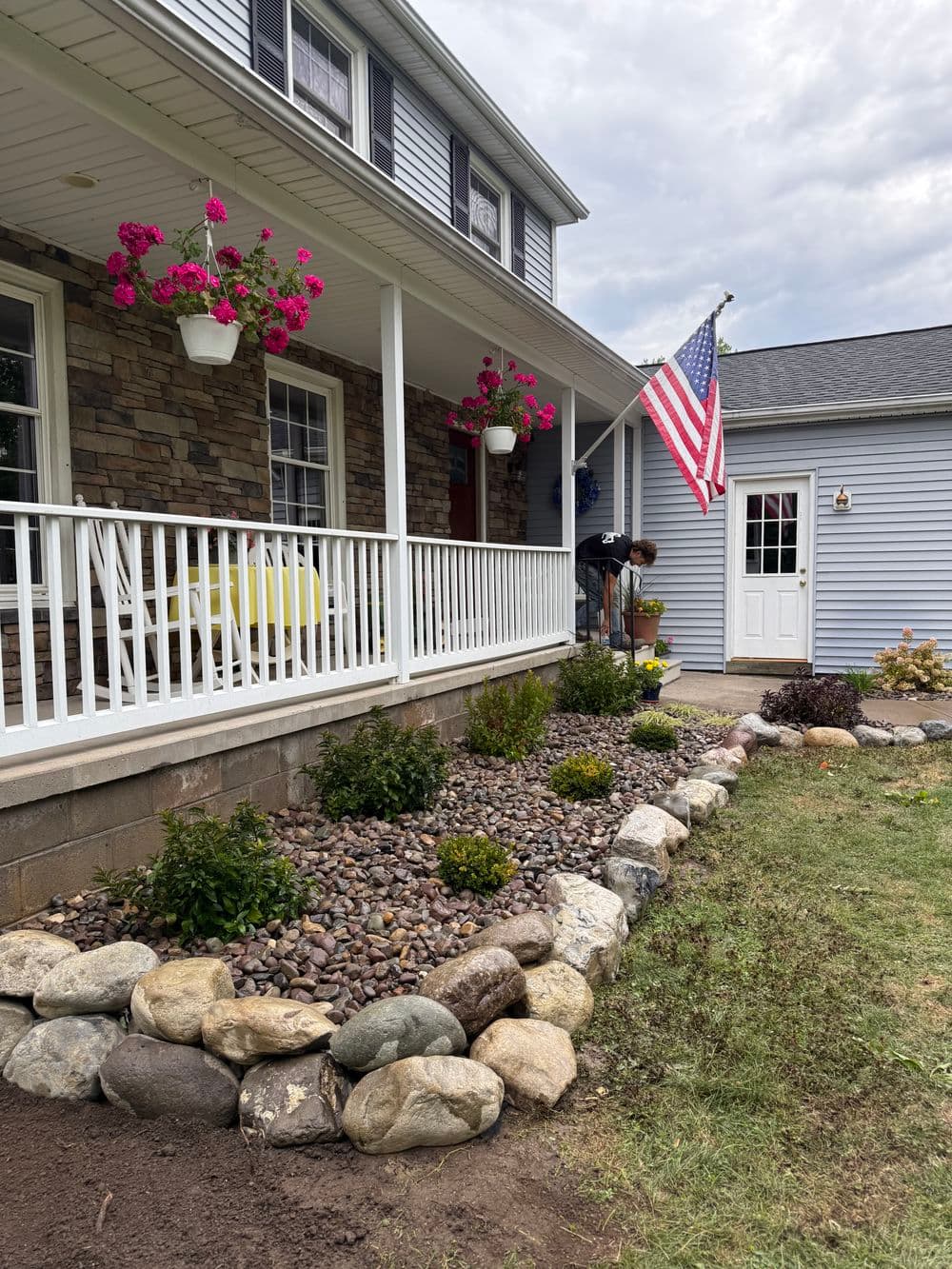 Charming house with American flag, flower pots, and landscaped stone garden in front yard.