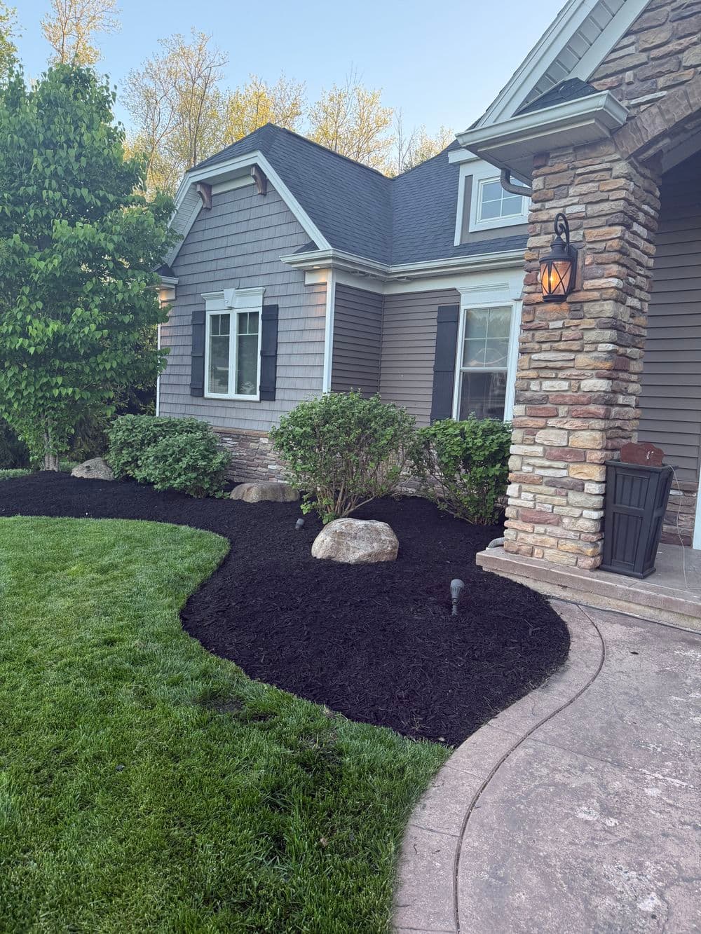 Front yard landscaping with fresh black mulch, rocks, and a well-maintained home exterior.